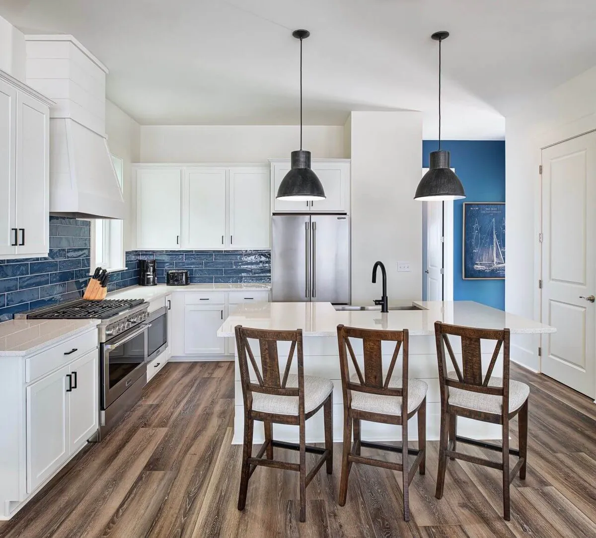 A stylish chef-inspired kitchen with a large island countertop, striking blue backsplash, pendant lighting, and sleek stainless steel appliances. The space feels welcoming and functional, designed for both cooking and entertaining guests.