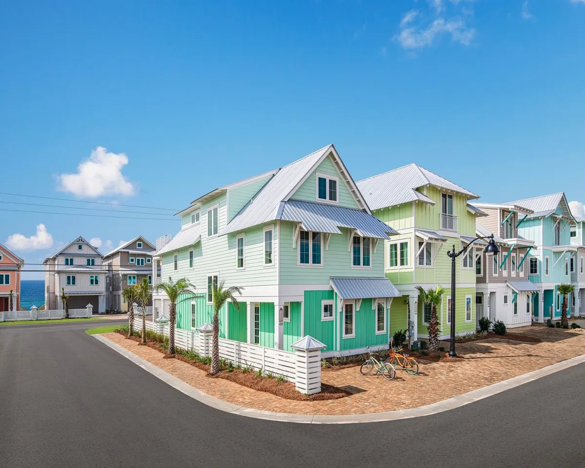 A cheerful exterior scene showcasing colorful houses with balconies facing a paved walkway lined with palm trees and bicycles. The setting evokes a leisurely neighborhood vibe, with spaces ideal for sunset views and community connection.