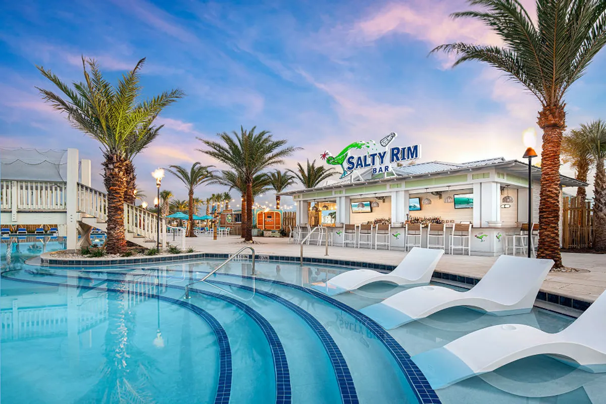 A festive poolside scene featuring the Salty Rim Bar & Grill with clear signage, bar seating, and guests enjoying food and drinks. The pool has partially submerged lounge chairs, surrounded by palm trees, and a staircase leading to an elevated deck. The mood is lively and social, with the bar playing a central role.