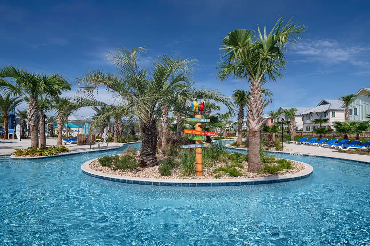 This image features the resort’s meandering lazy river with clear blue water, surrounded by lush palm trees and tropical landscaping. Blue lounge chairs line the poolside, and a colorful directional signpost adds a fun, whimsical touch. Families and friends are seen floating in the lazy river and relaxing under the sun.